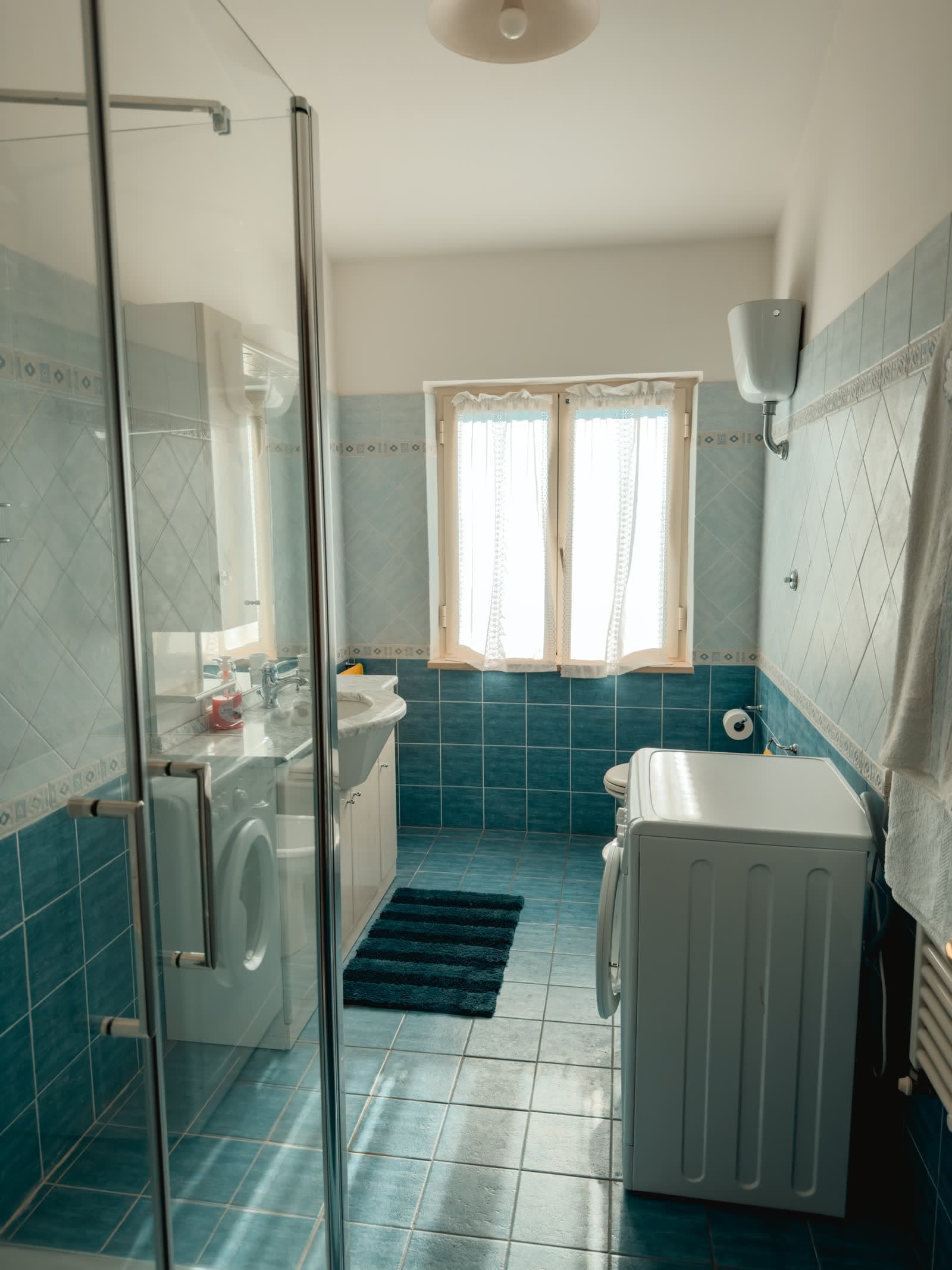 The bathroom with pale blue tiles, shower and washing machine