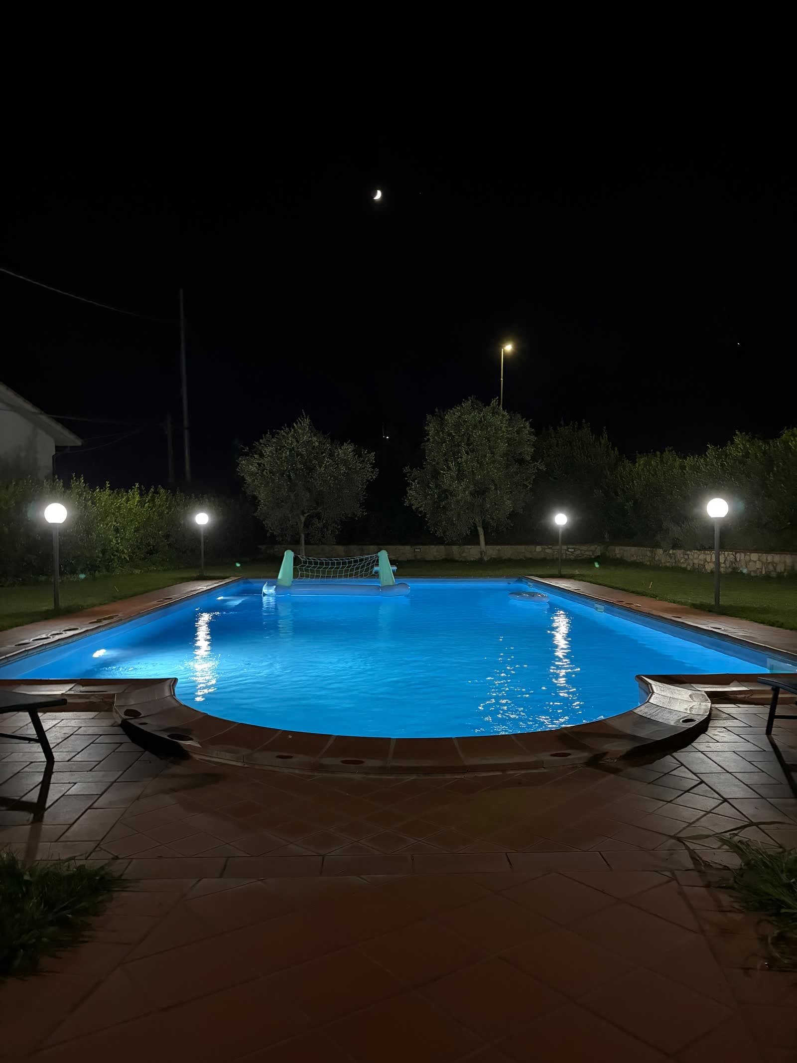 The pool lit up at night beneath a crescent moon